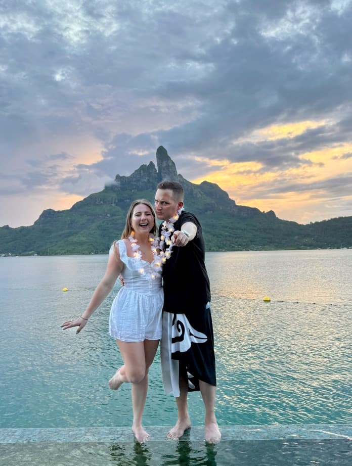 Thomas and Victoria standing in shallow water at sunset with a mountain peak behind them.
