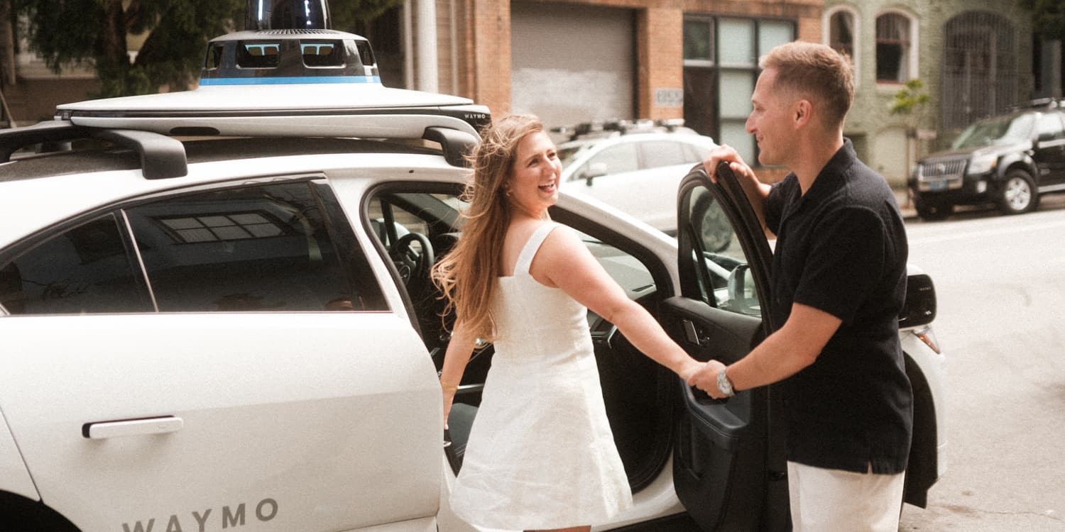 Victoria laughing with Thomas while holding hands beside a Waymo in San Francisco.